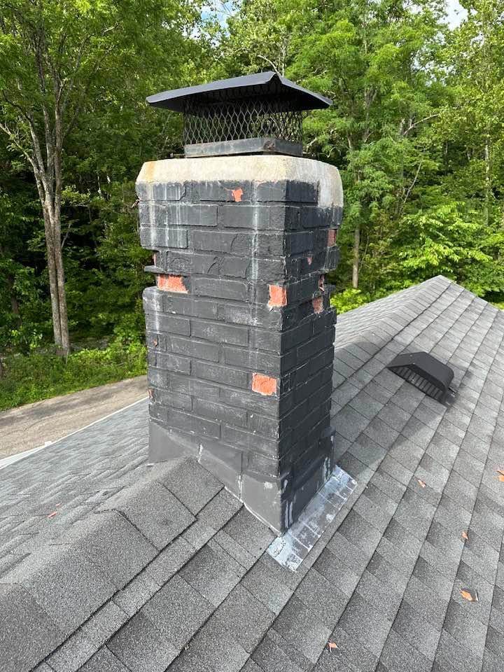 Dark-painted brick chimney with several brick faces spalled off exposing orange clay, Dallas TX