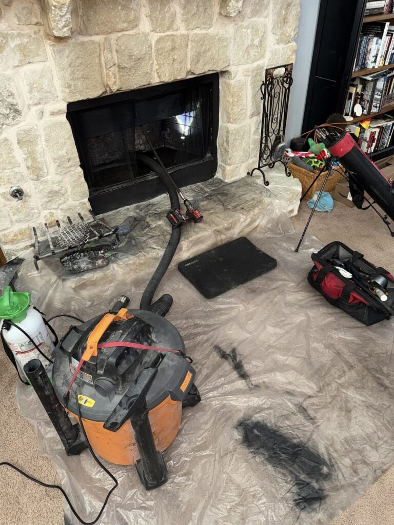 Chimney sweeping setup with a vacuum, hose, tools and protective floor covering.