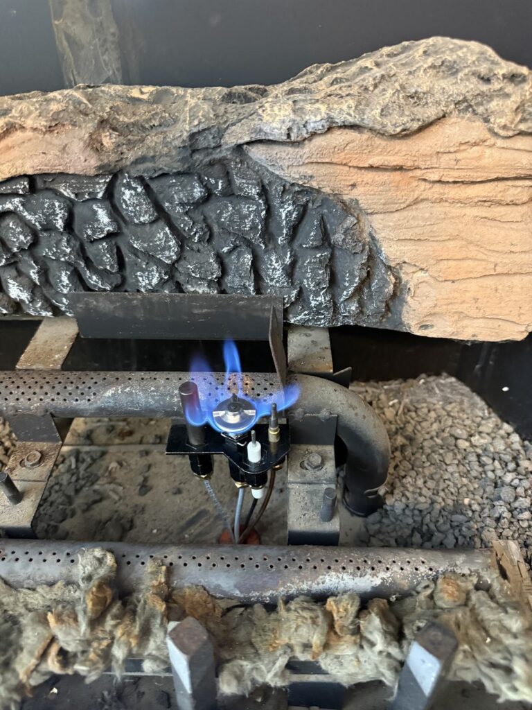 Gas fireplace pilot assembly with a visible blue pilot flame.